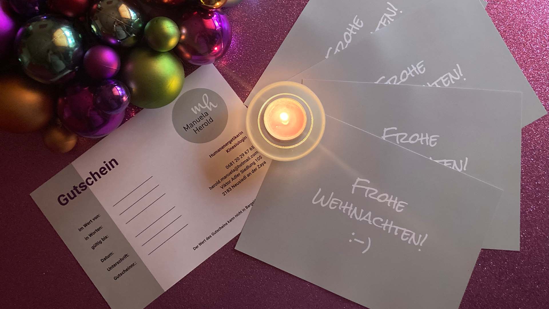 Foto von Gutscheinen für Sitzungen von Manuela Herold. Diese liegen auf einer lila glitzernden Oberfläche. Links oben sind Weihnachtskugeln, auf den Gutscheinen steht eine Kerze.