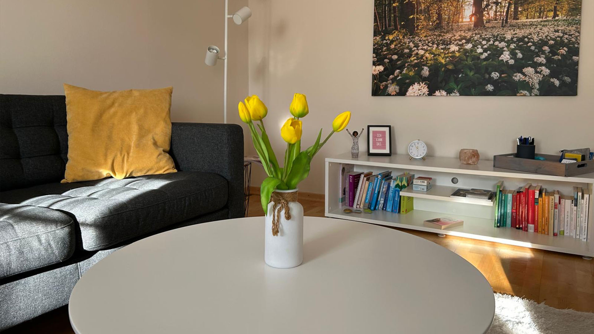 Praxisraum Bild. Links sieht man eine Couch, rechts ein Bücherregal. Über dem Bücherregal ist ein Bild einer Wiese.