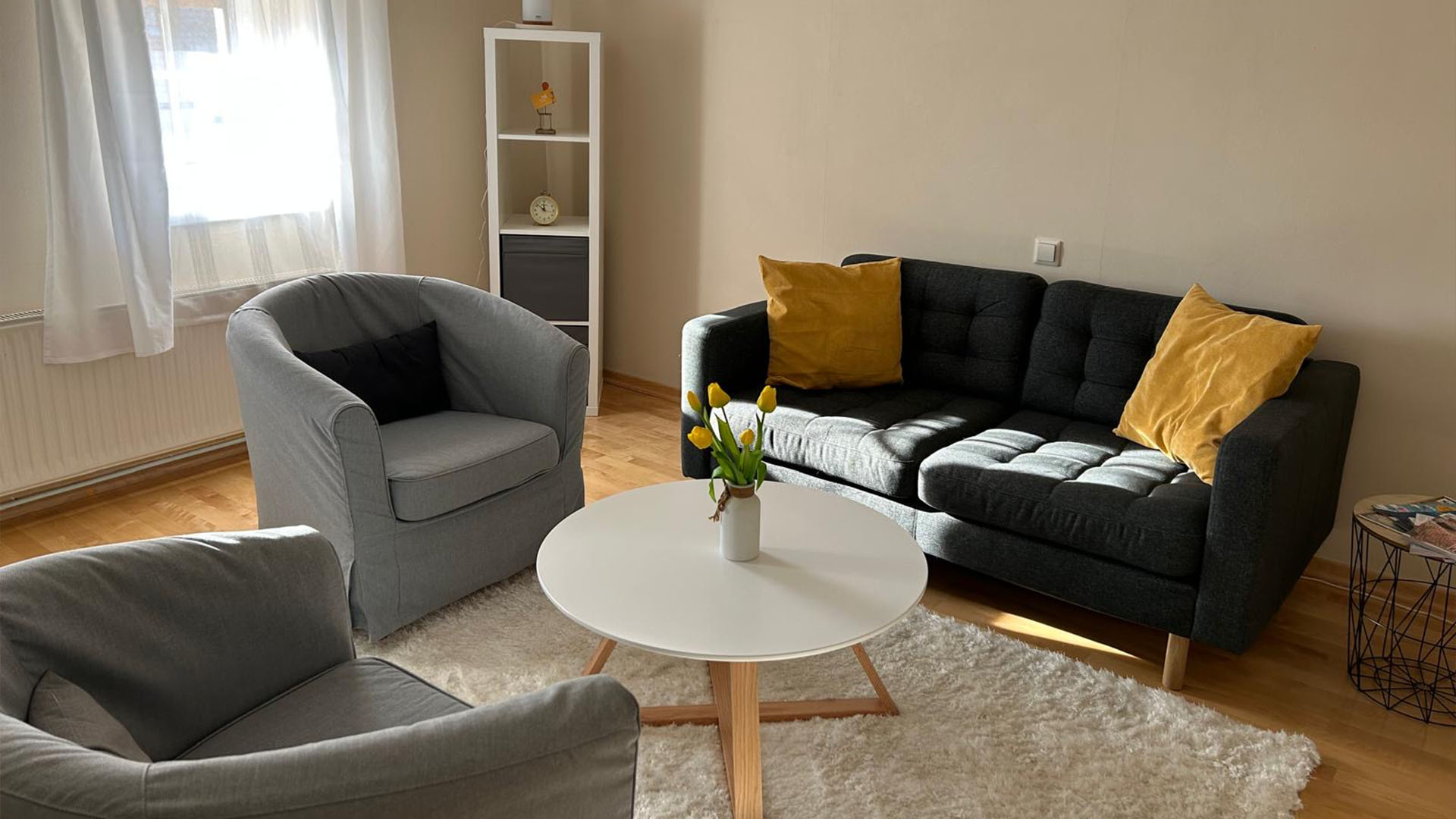 Bild des Praxisraums: Man sieht einen runden Kaffeetisch, um den herum eine dunkle, gemütliche Couch und zwei Sessel stehen.